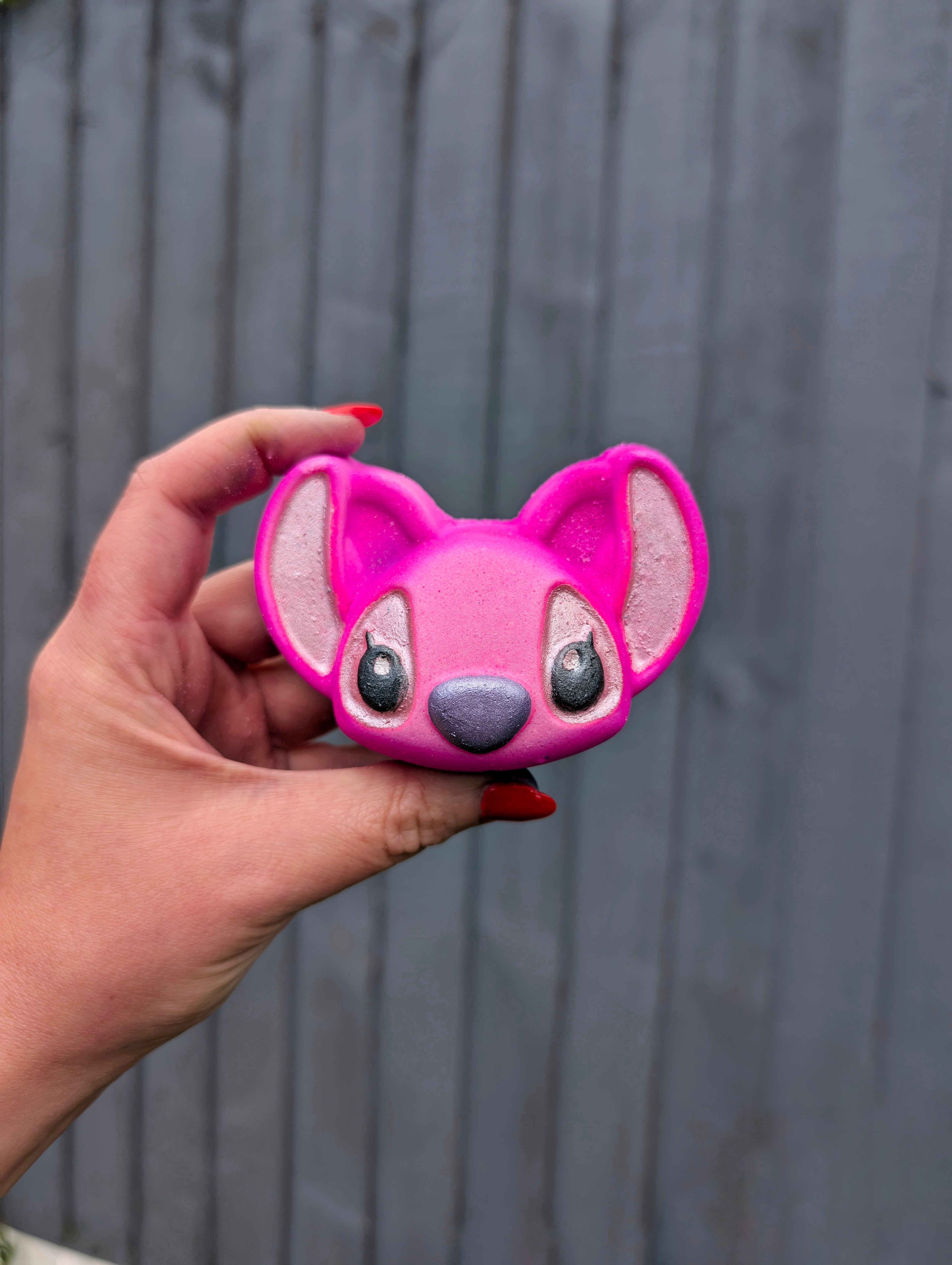 Angel experiment 628 shaped bath bomb, coloured pink with a grey fence in the background.