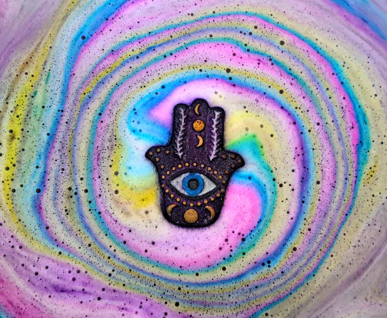 Hand holding a hamsa hand shaped bath bomb from Fizz Bomb Cosmetics, featuring purple, white, and gold detailing – a fun, mystical themed bath treat perfect for gifting or relaxing self care days.