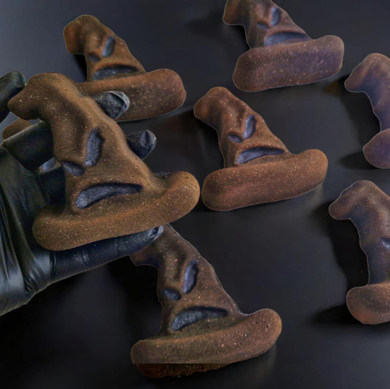 Bath bombs designed to look like a character's hat from Harry Potter, placed on a black surface, with one being held by a hand wearing a black glove.