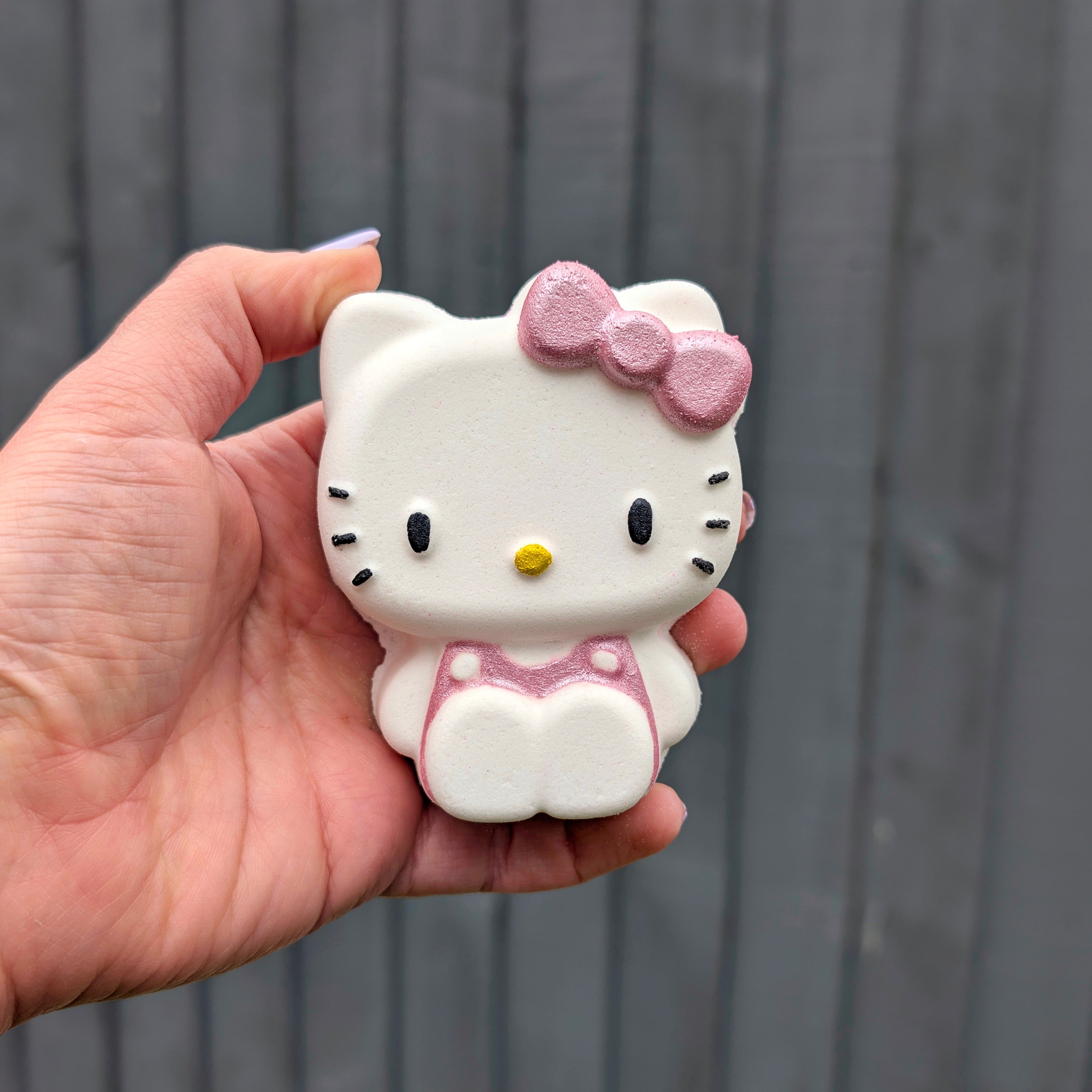 Hand holding a Kawaii Hello Kittybath bomb from Fizz Bomb Cosmetics, featuring pink and yellow detailing – a fun, Hello Kitty themed bath treat perfect for gifting or relaxing self care days.