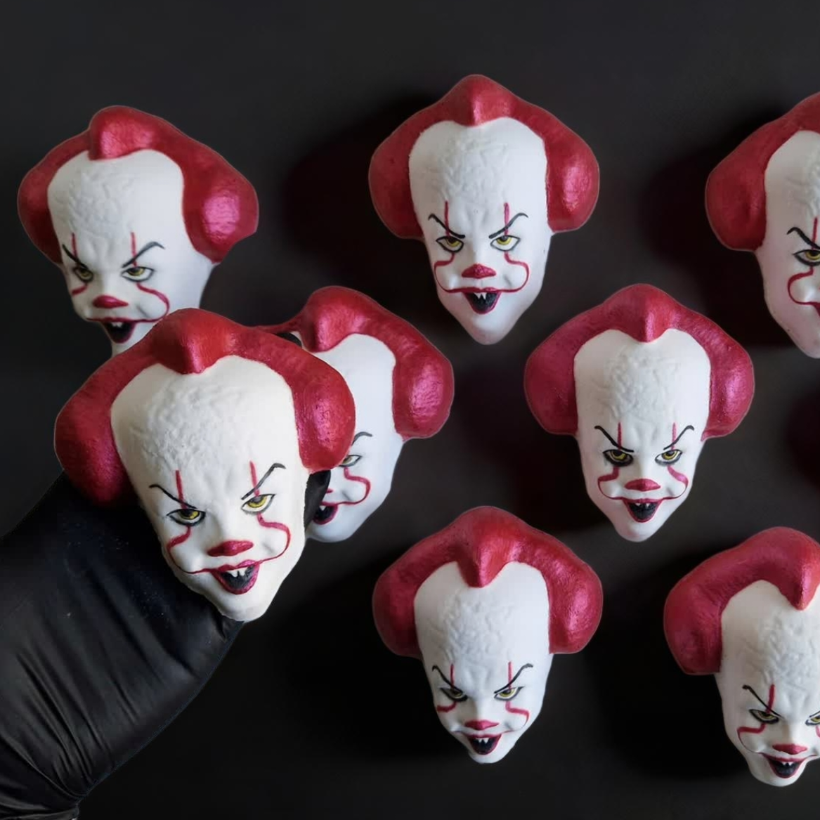 Hand holding an IT Clown face shaped bath bomb from Fizz Bomb Cosmetics, on a black background. Featuring red and black detailing – a fun, IT Clown themed bath treat perfect for gifting or relaxing self-care days.