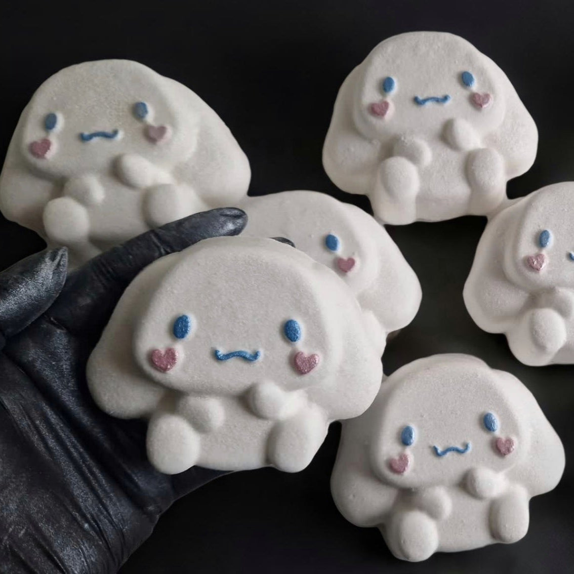 Hand holding a kawaii cinnamoroll shaped bath bomb from Fizz Bomb Cosmetics, on a black background. Featuring pin and blue detailing – a fun, kawaii themed bath treat perfect for gifting or relaxing self-care days.
