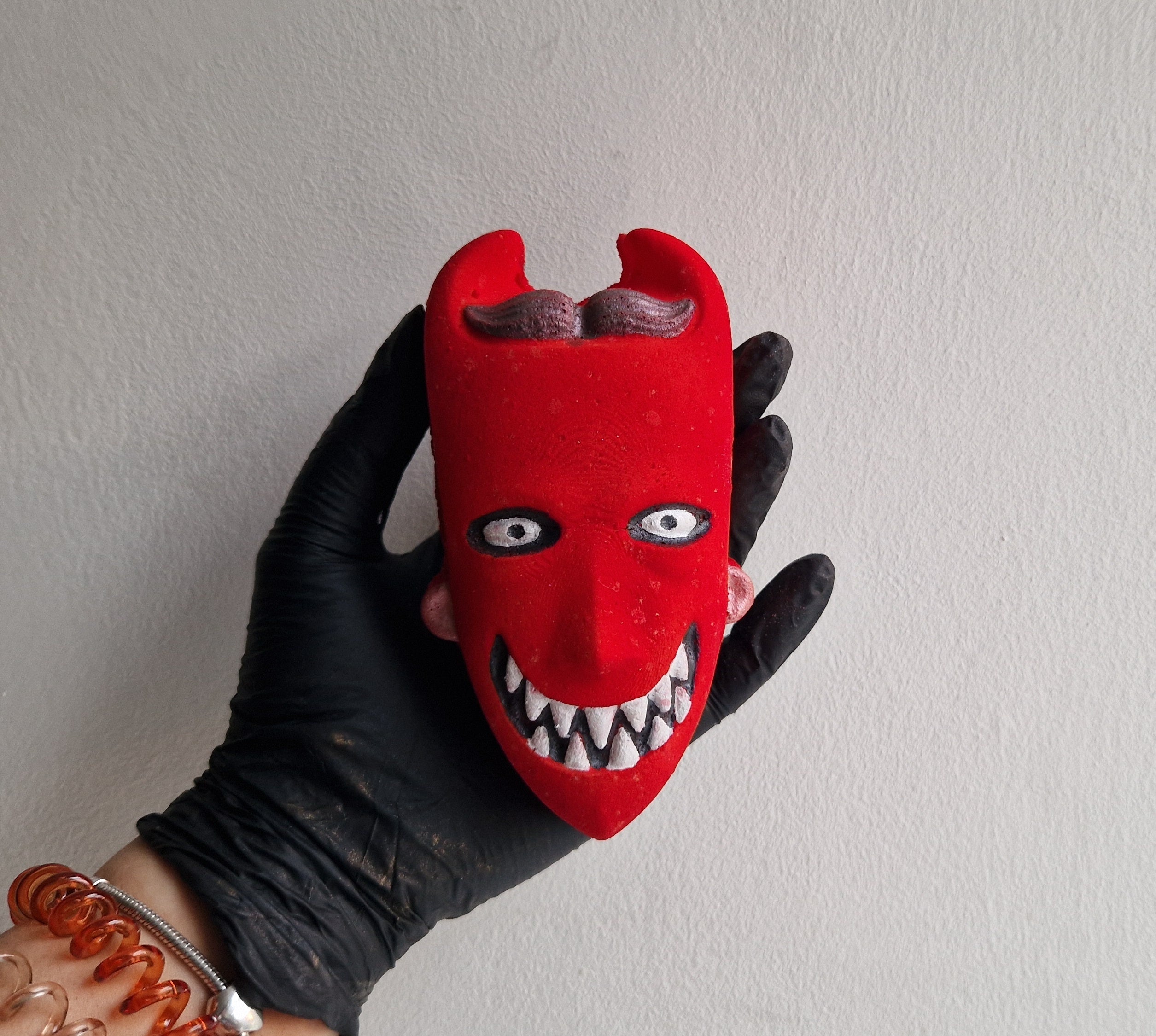 A hand holding a red bath bomb shaped like a trick or treater with a playful face.