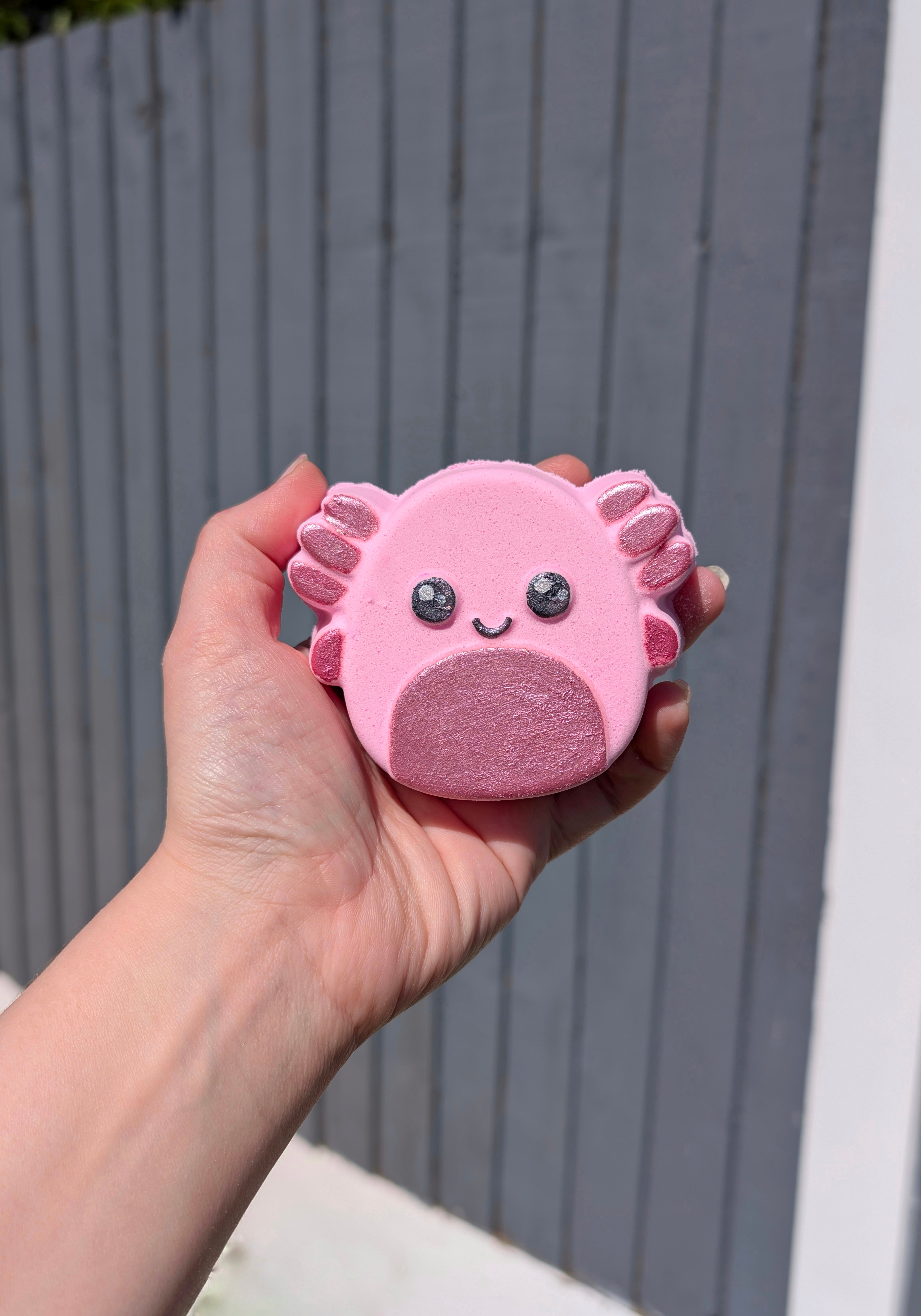 Hand holding an axolotl shaped bath bomb from Fizz Bomb Cosmetics, featuring pink and black detailing – a fun, squishmallow themed bath treat perfect for gifting or relaxing self care days.