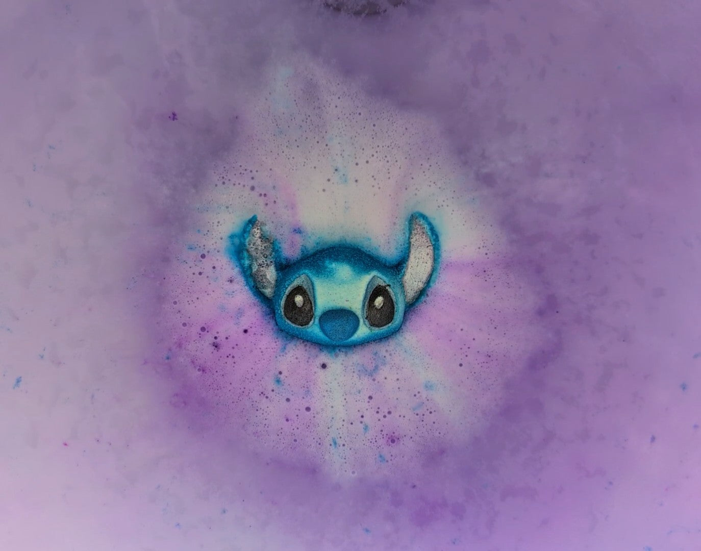 A stitch character shaped bath bomb from Fizz Bomb Cosmetics, fizzing in the bath. Featuring blue and black detailing – a fun, hawaii stitch themed bath treat perfect for gifting or relaxing self-care days.
