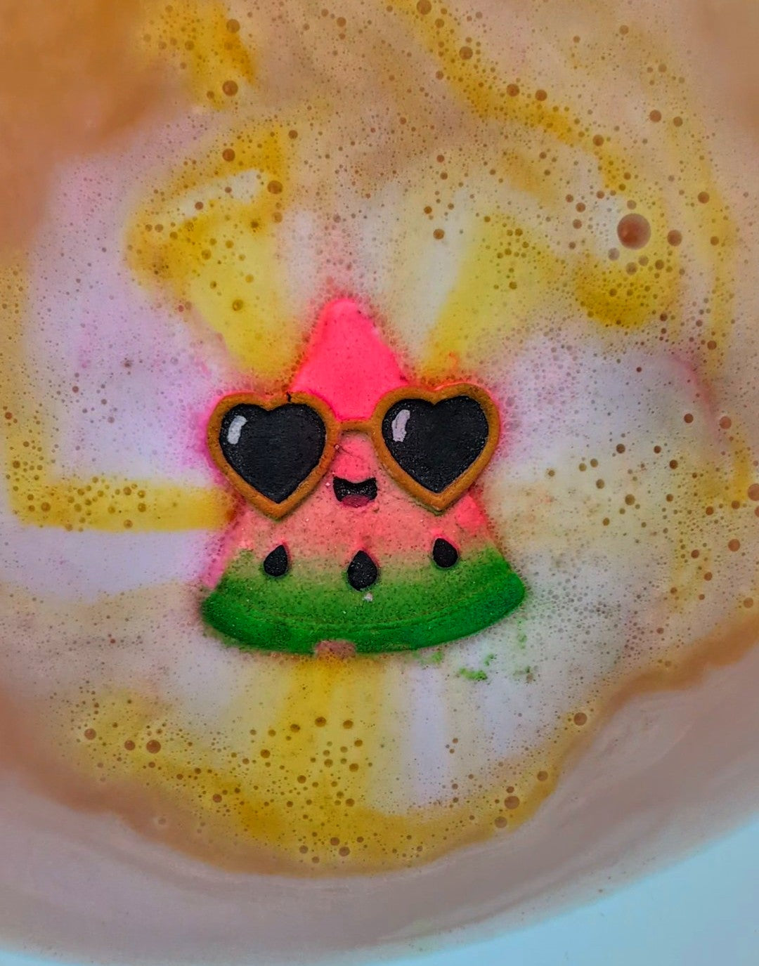 Watermelon slice shaped bath bomb in use from Fizz Bomb Cosmetics, featuring black and gold detailing and yellow bursting colour fizzing into the water– a fun, summer themed bath treat perfect for gifting or relaxing self care days.