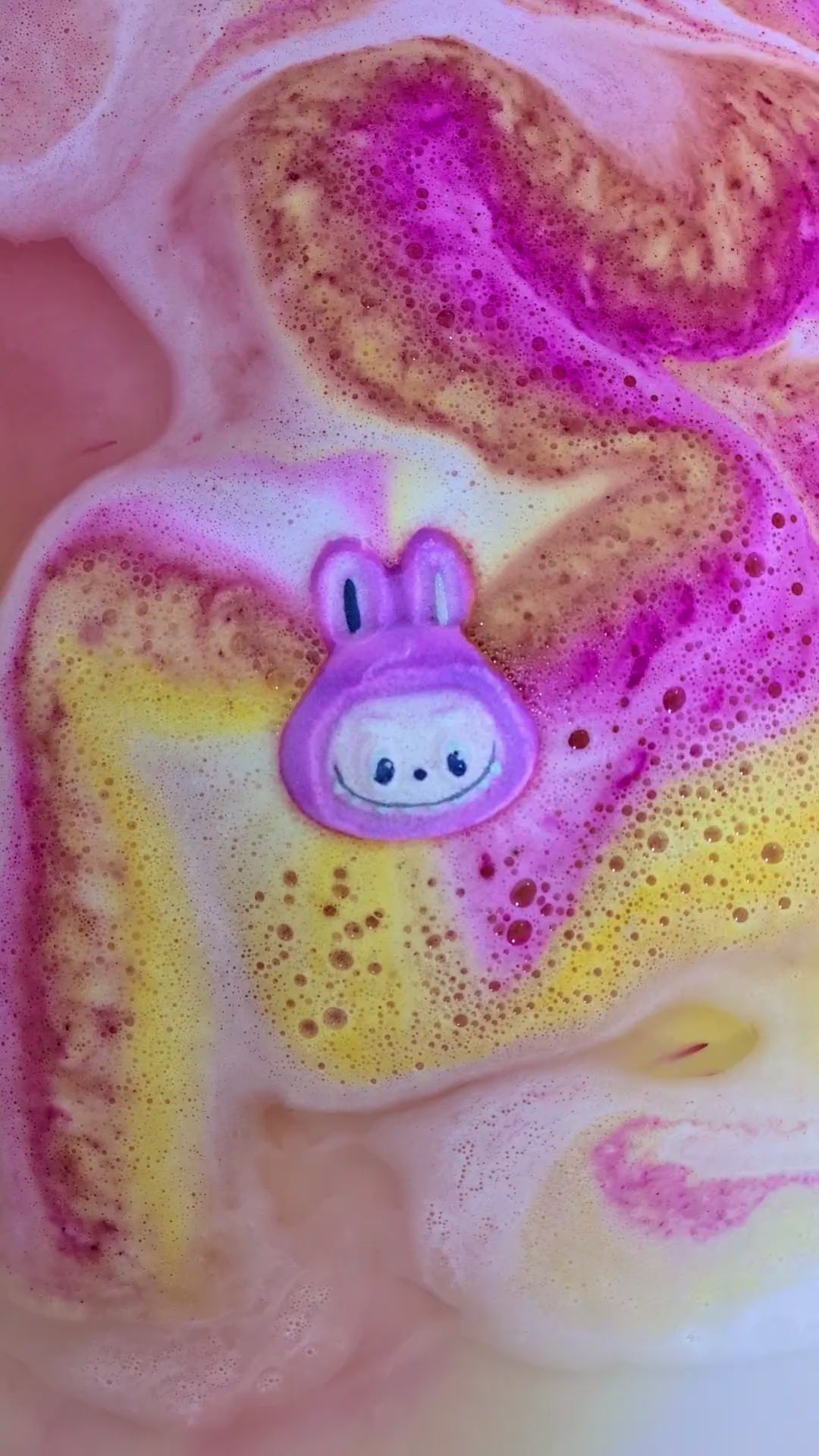 Pink labubu shaped bath bomb in use in the bath, with yellow and pink colours bursting out.
