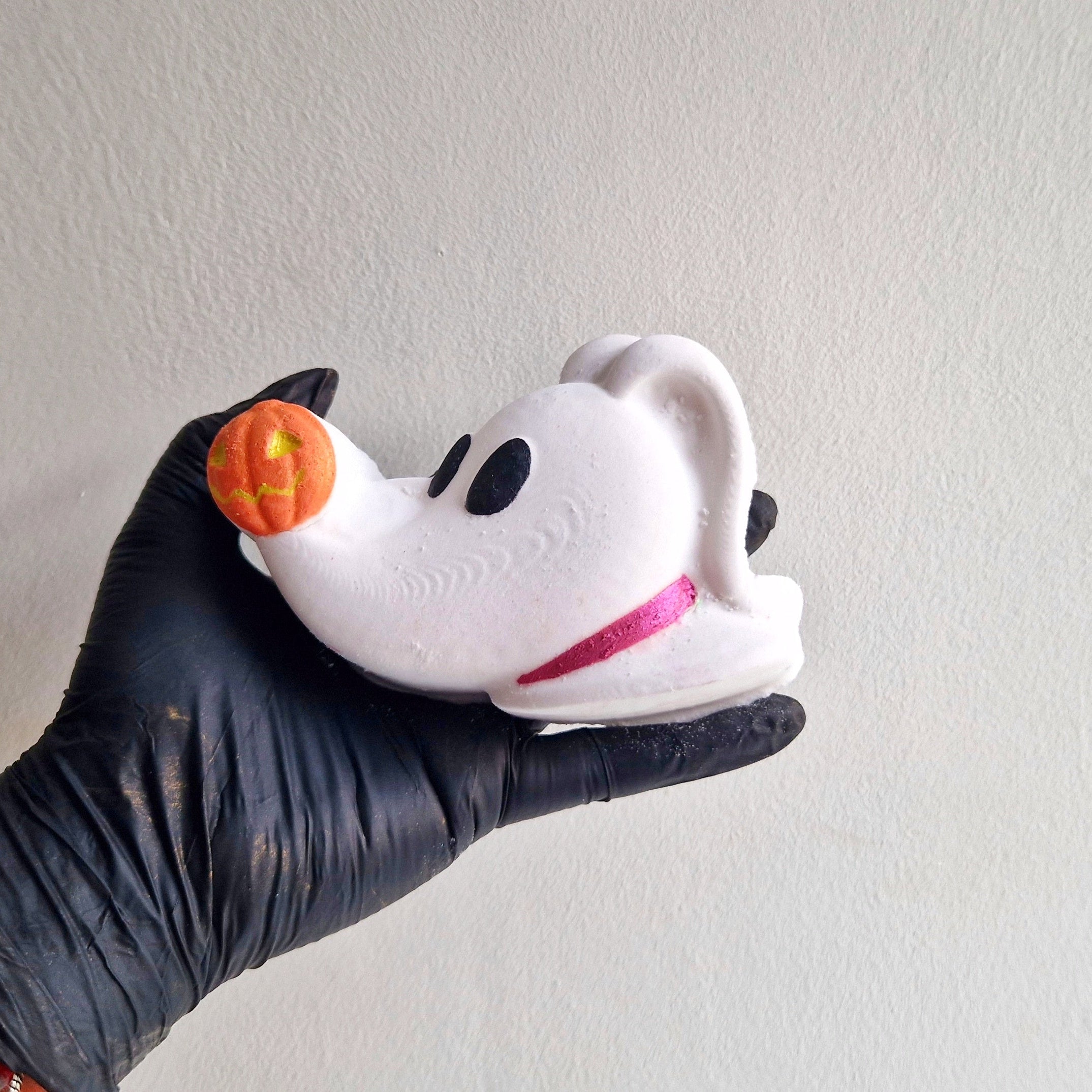 A bath bomb shaped like zero dog with a white body and black details, held in a person with a black glove.