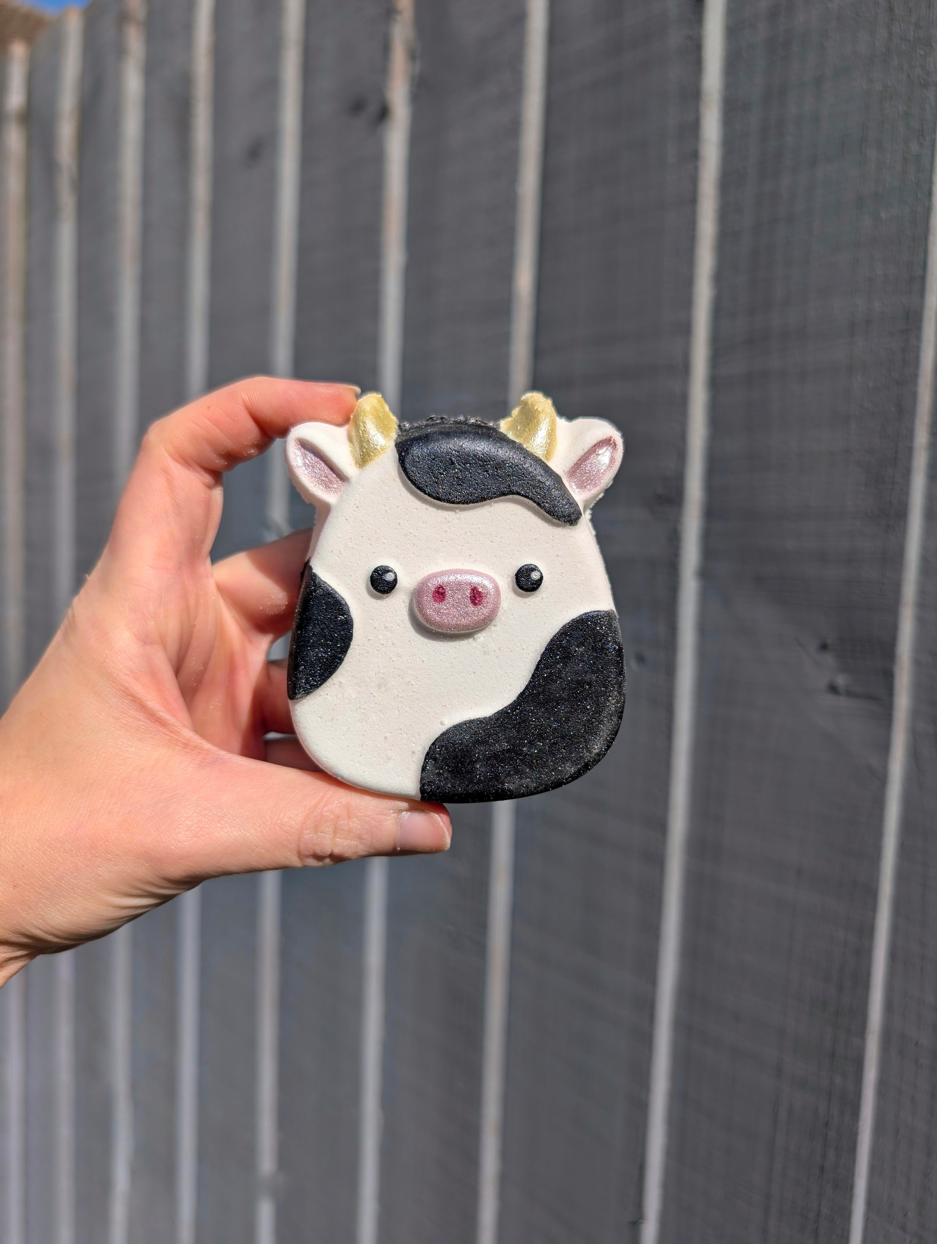 Hand holding a cow-shaped bath bomb against a wooden fence background