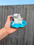 Hand holding a dolphin bath bomb on a blue wave, against a wooden fence background