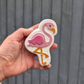 Hand holding a flamingo shaped bath bomb from Fizz Bomb Cosmetics, featuring pink, white, and gold detailing – a fun, tropical themed bath treat perfect for gifting or relaxing self care days.