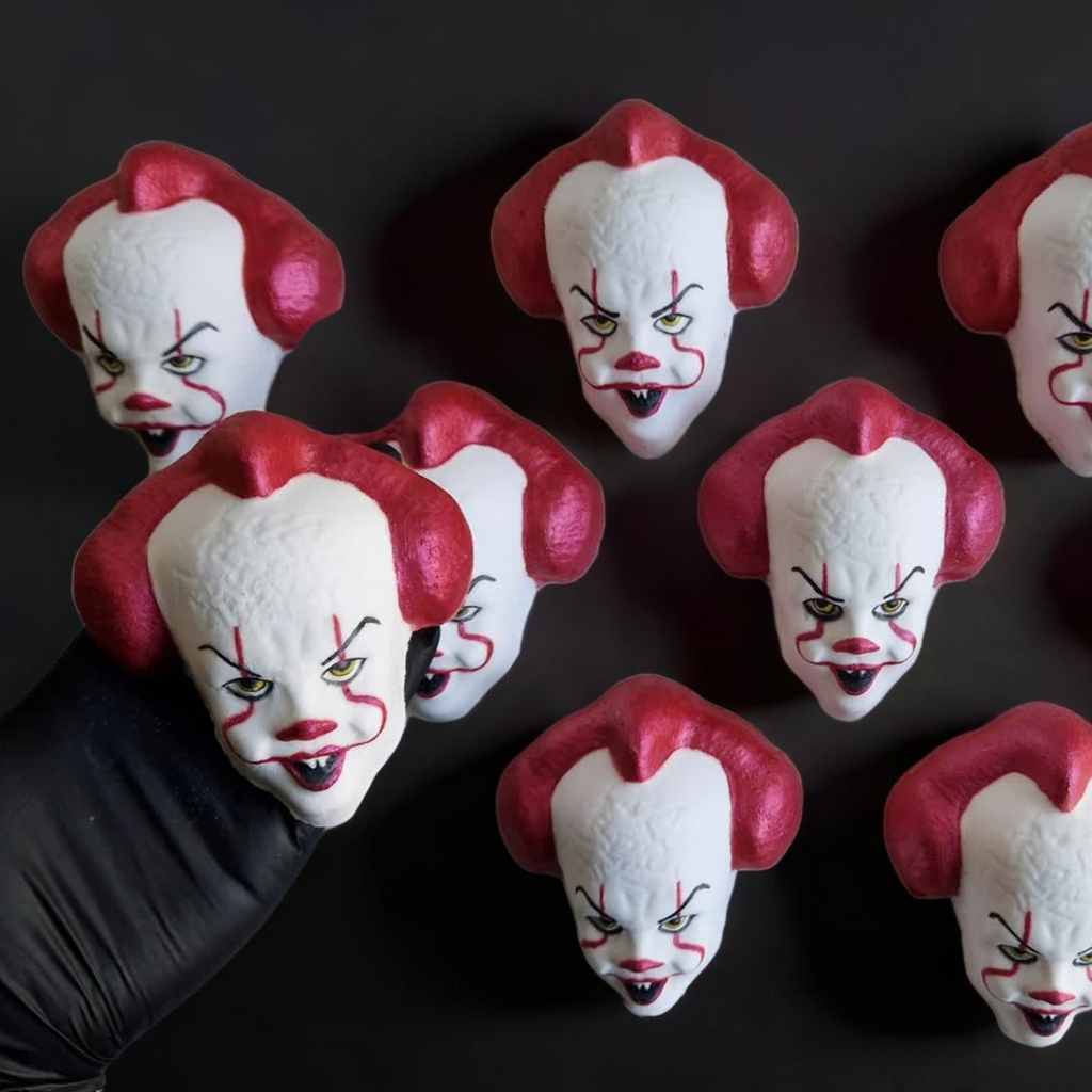 Hand holding an IT Clown face shaped bath bomb from Fizz Bomb Cosmetics, on a black background. Featuring red and black detailing – a fun, IT Clown themed bath treat perfect for gifting or relaxing self-care days.