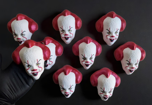 Hand holding an IT Clown face shaped bath bomb from Fizz Bomb Cosmetics, on a black background. Featuring red and black detailing – a fun, IT Clown themed bath treat perfect for gifting or relaxing self-care days.