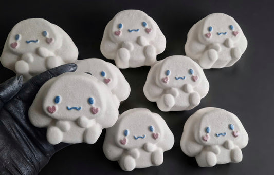 Hand holding a kawaii cinnamoroll shaped bath bomb from Fizz Bomb Cosmetics, on a black background. Featuring pin and blue detailing – a fun, kawaii themed bath treat perfect for gifting or relaxing self-care days.