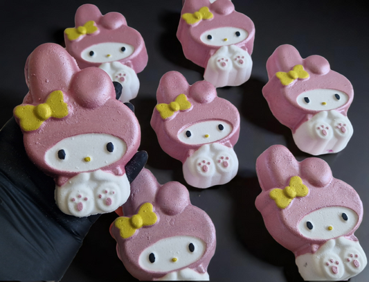 Hand holding a kawaii my melody shaped bath bomb from Fizz Bomb Cosmetics, on a black background. Featuring pink and yellow detailing – a fun, kawaii themed bath treat perfect for gifting or relaxing self-care days.