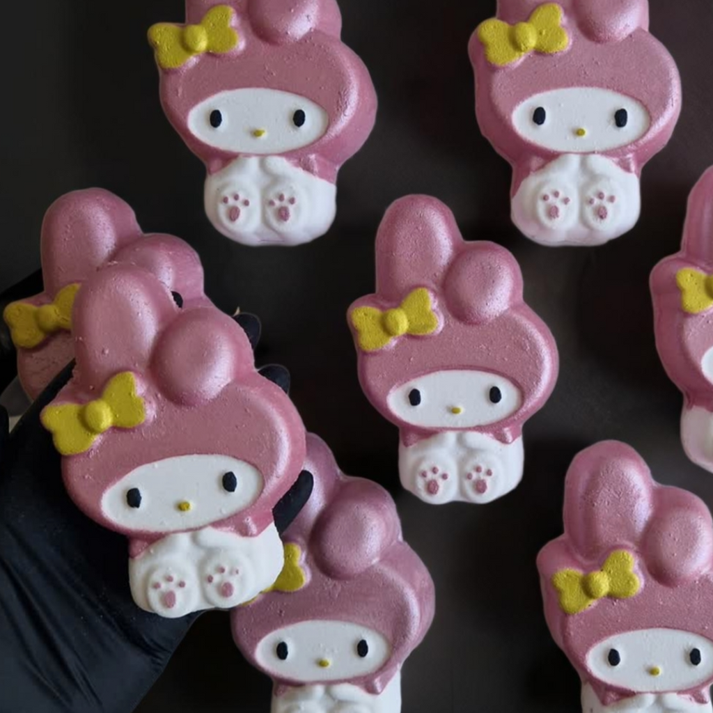A kawaii my melody shaped bath bomb from Fizz Bomb Cosmetics, on a black background. Featuring pink and yellow detailing – a fun, kawaii themed bath treat perfect for gifting or relaxing self-care days.