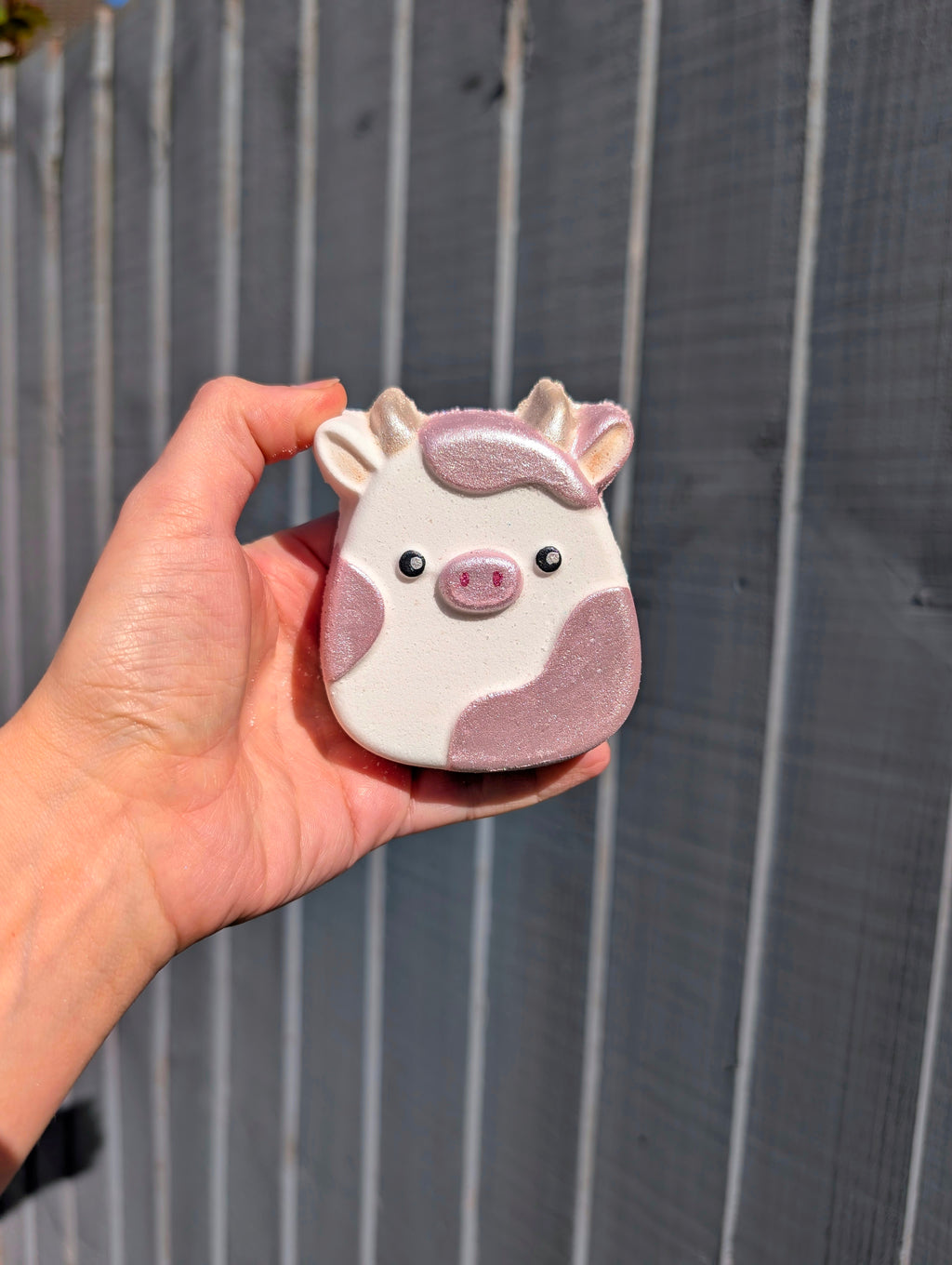 Hand holding a small cow shaped shaped object against a wooden fence background