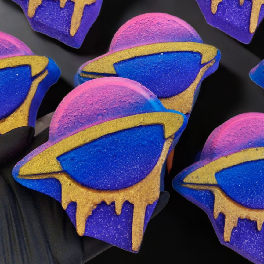 A collection of bath bombs shaped like planets with a gold dripping paint effect in vibrant colours, displayed on a dark background.