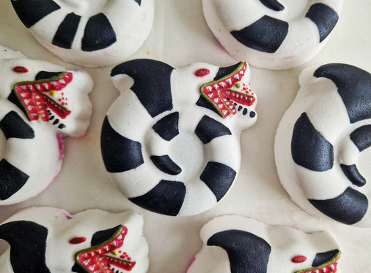 A close up of a sandworm shaped bath bomb from Fizz Bomb Cosmetics, on a black background. Featuring red and black detailing – a fun, beetlejuice themed bath treat perfect for gifting or relaxing self-care days.