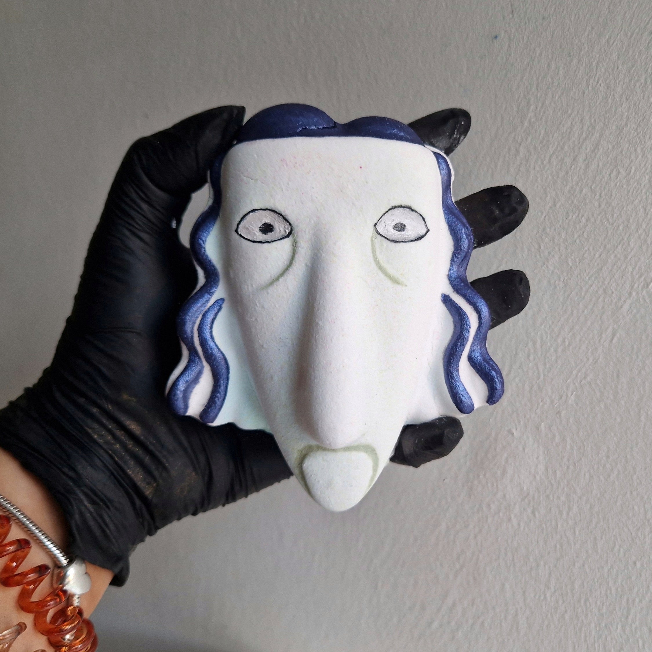 A hand holding a bath bomb shaped like a NBC Shock character with a prominent white face and blue hair.