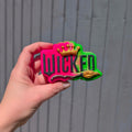 Hand holding a wicked shaped bath bomb from Fizz Bomb Cosmetics, featuring bright pink, green, black and gold detailing – a fun, wicked themed bath treat perfect for gifting or relaxing self care days.