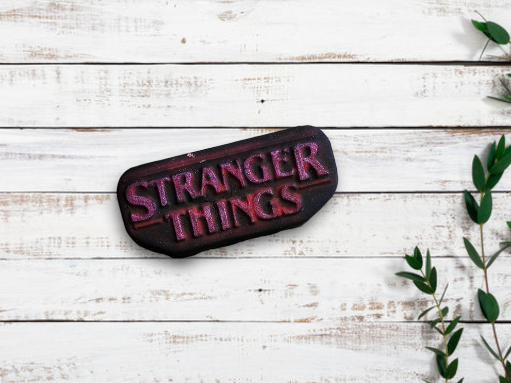 A bath bomb with 'STRANGER THINGS' text on it, placed on a wooden surface, with a few leaves of a plant to the side.